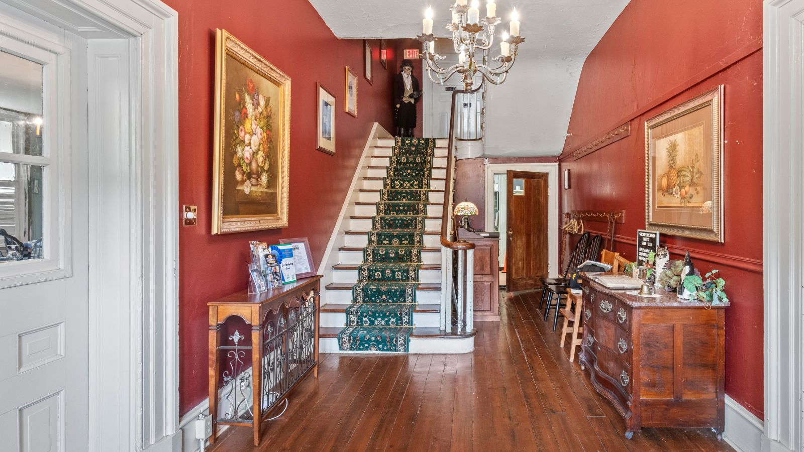 Front foyer of a home with hardwood floors, red walls, antique furniture and staircase with a green runner