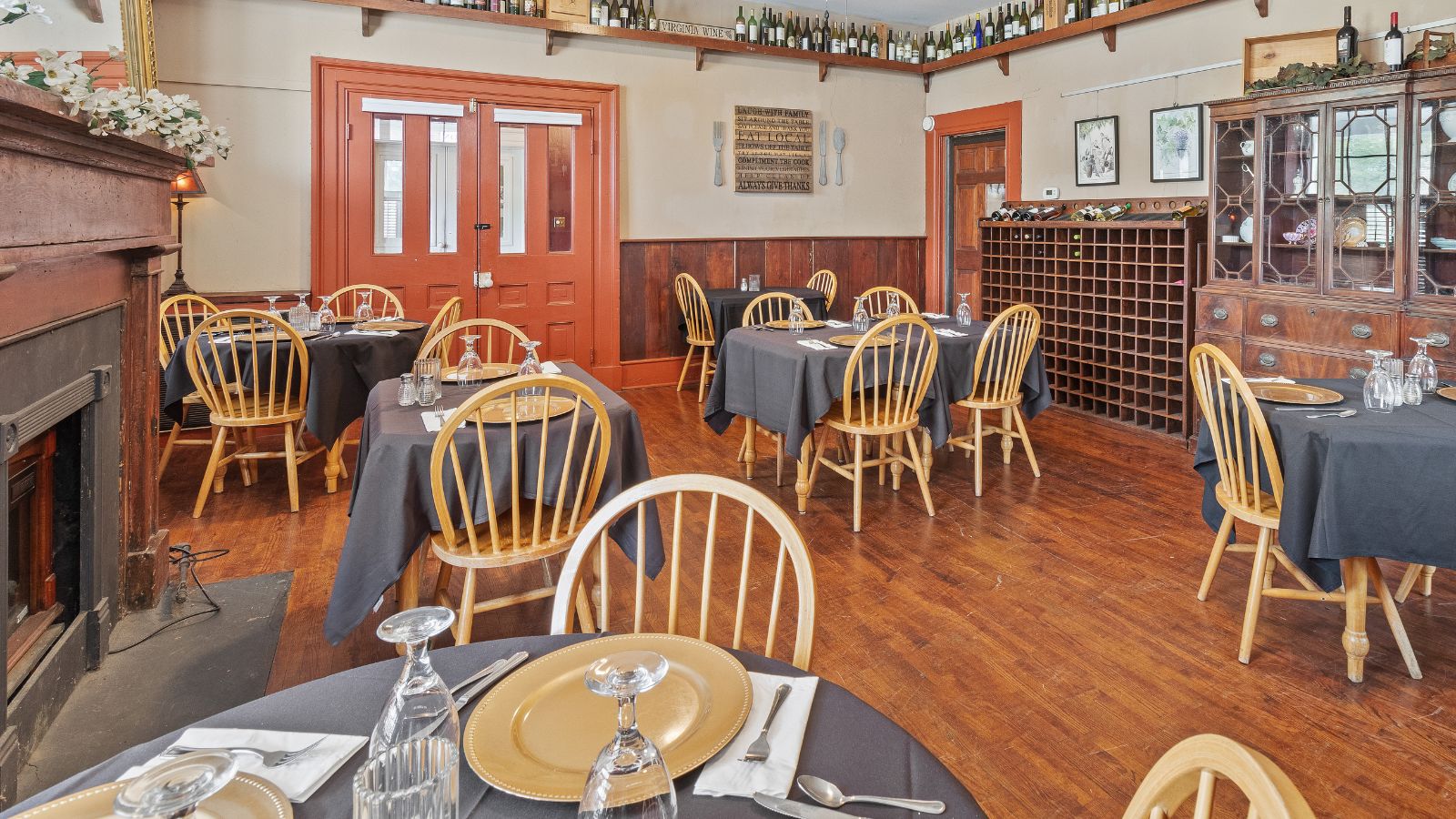 Large dining room with a fireplace, hardwood floors and several tables set with gold plates, grey tablecloths and glasses