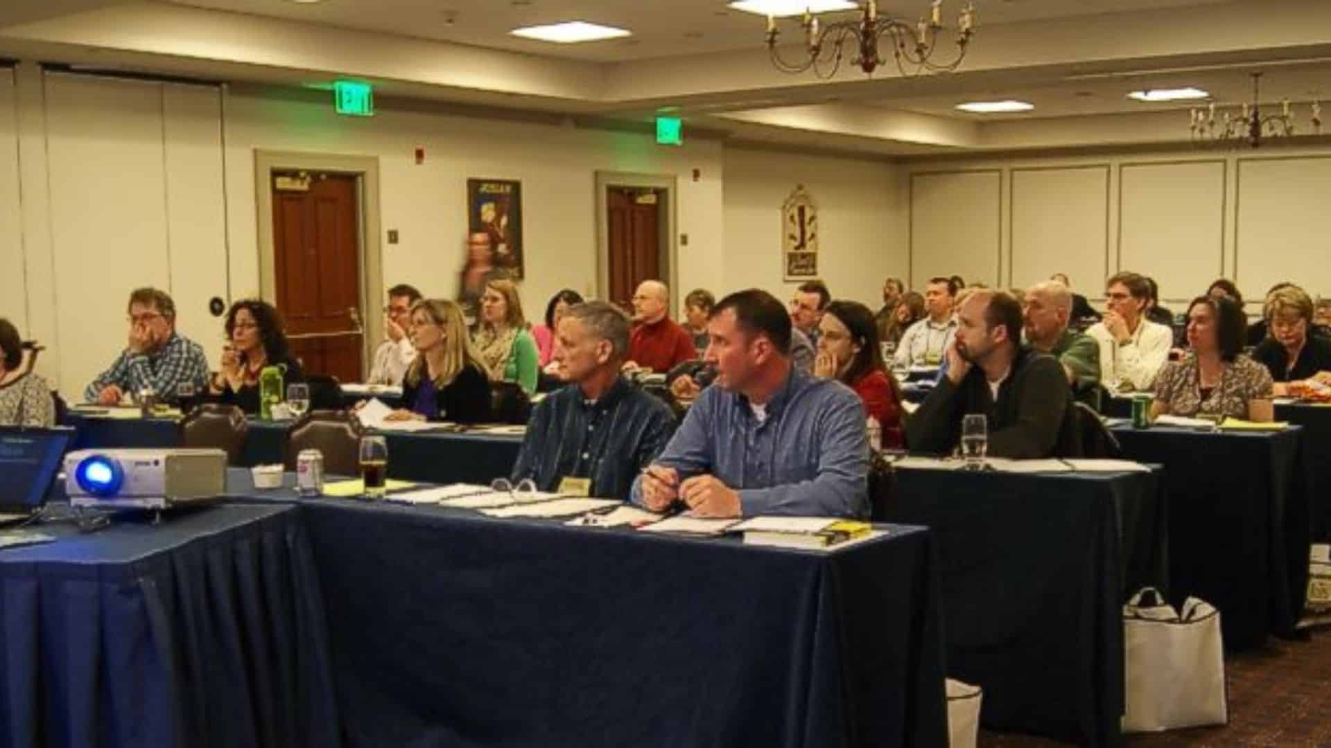 A group of people sitting at blue tables in a conference room