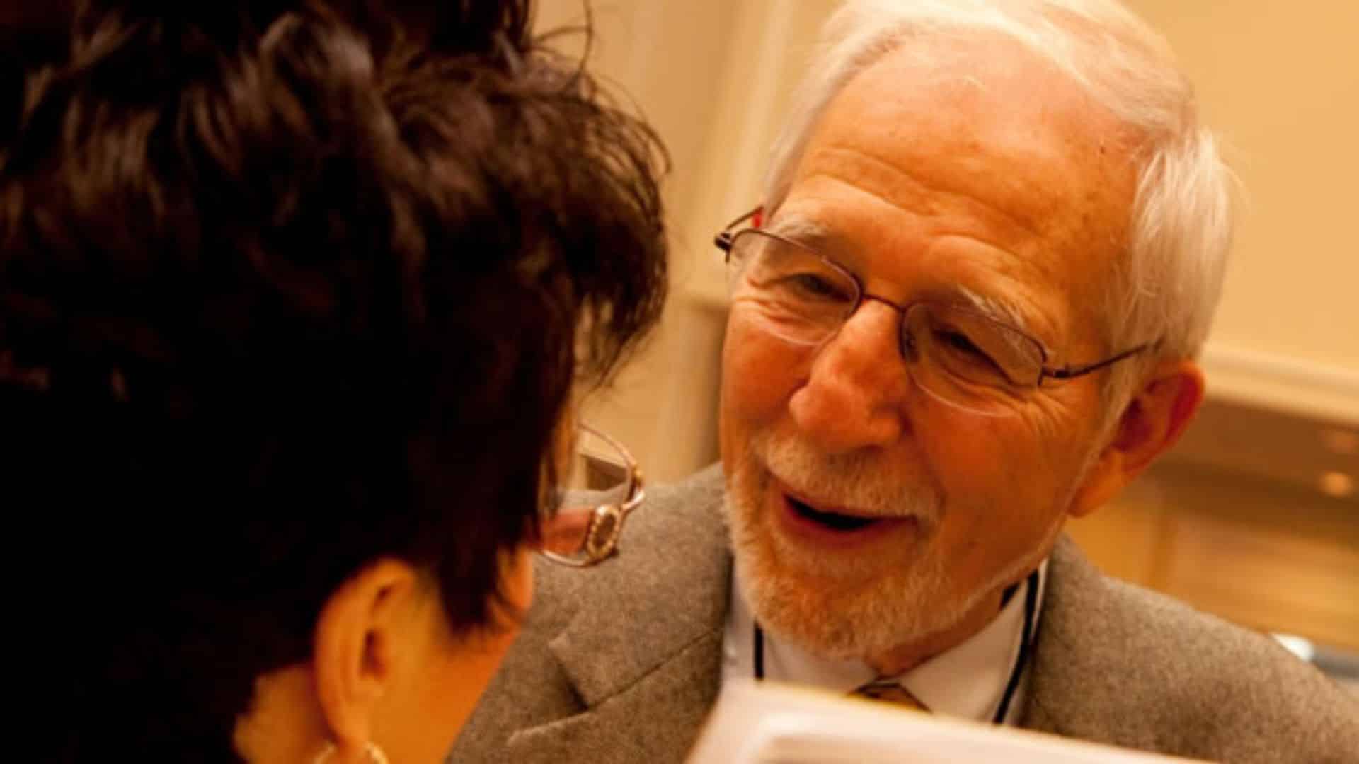 A gentleman in glasses and a grey suit talking to a woman with dark hair