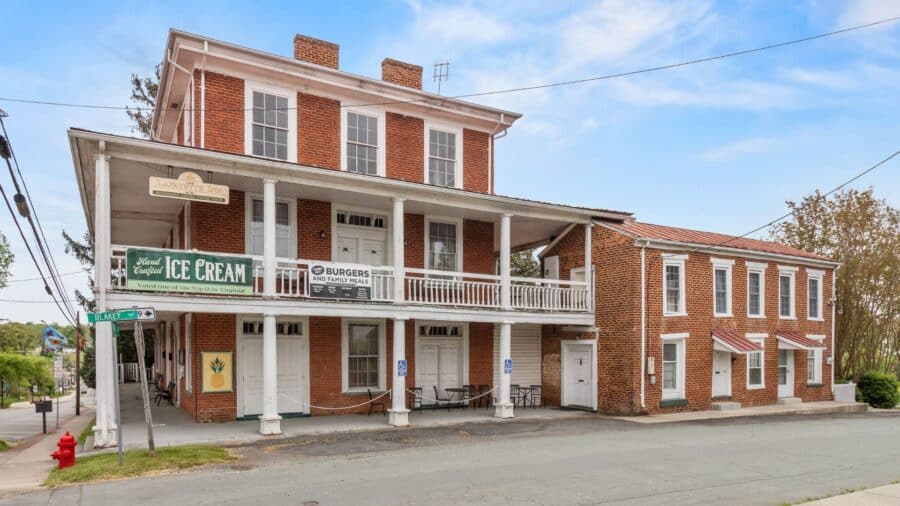 Large red brick two-story building with wrap around porch, lots of windows and ice cream banner on railing