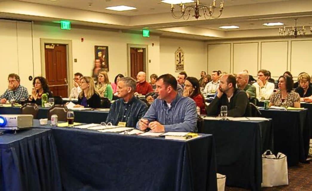 A group of people sitting at blue tables in a conference room