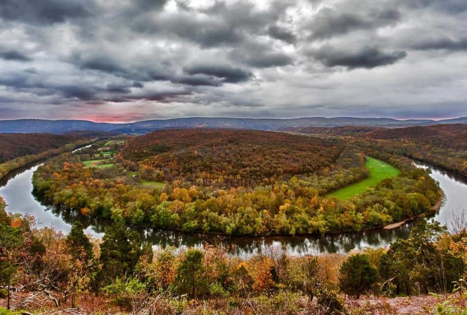 Curved river in the shape of a horseshoe surrounded by fall colored trees and cloudy skies above