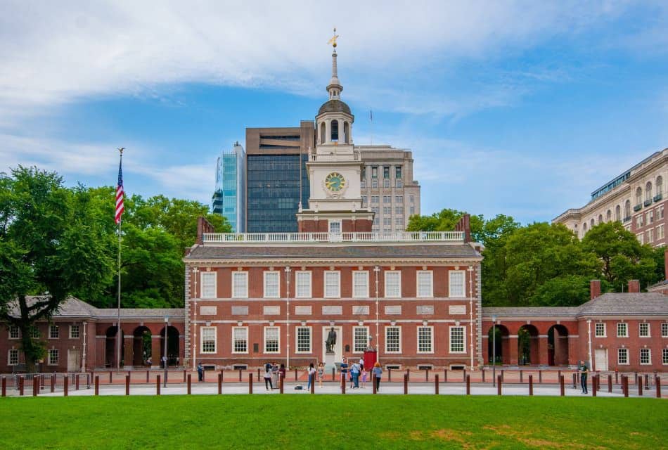 Large red brick city building with clock tower and people walking on a sidewalk in front