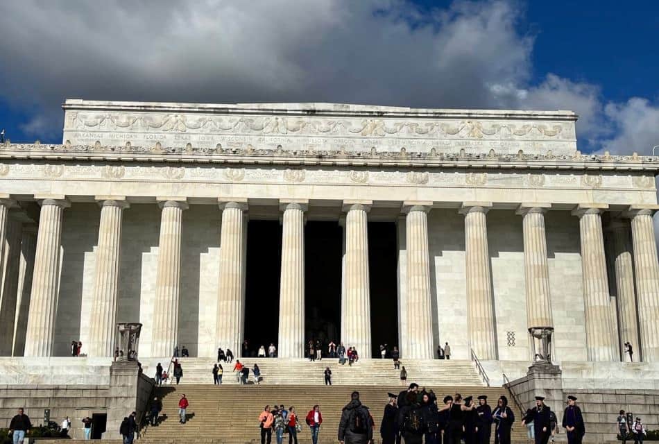 Large government building with rows of large columns and people milling around the front steps and sidewalks